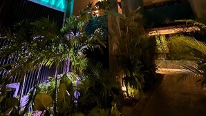 En moderne bygning med et neon-skilt der viser ”VOLTA” samt et poolområde med frodig beplantning omkring.