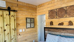 Una habitación con paneles de madera, una cama, un ventanal con celosía decorativa y obras de arte en las paredes.