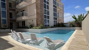 Un bâtiment moderne doté d’une piscine, de nombreux balcons et de chaises longues.