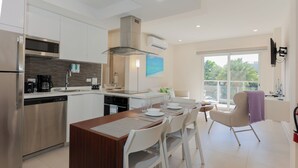 Une cuisine moderne équipée d’appareils électroménagers en acier inoxydable, un coin repas avec des chaises blanches et un balcon offrant une vue agréable.