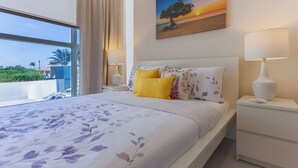 Une chambre d’hôtel avec un grand lit, une table de chevet, une lampe et un tableau représentant un coucher de soleil.