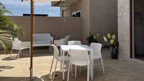 Een terras buiten met witte meubels, een beige parasol en een potplant.