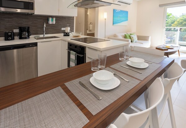 Een moderne keuken met een centraal eiland, roestvrijstalen apparatuur en een eethoek met witte stoelen en een tafel gedekt voor vier personen.