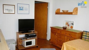Une petite pièce meublée, équipée d’une télévision, d’une armoire en bois et d’un tableau encadré accroché au mur.