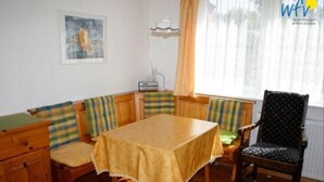 Un coin repas avec une table et des bancs, un radiateur, un tableau accroché au mur et une fenêtre avec des rideaux.
