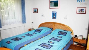 Une chambre double avec deux lits simples, une tête de lit en bois, une fenêtre avec des rideaux, une petite table de chevet avec une lampe et un mur décoré de tableaux encadrés.