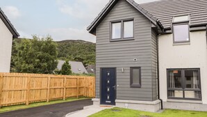 Una casa moderna de dos pisos con fachada gris oscuro, una puerta principal azul oscuro y un pequeño jardín delantero con valla de madera.