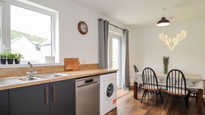 Una cocina moderna con lavavajillas, encimera de madera, fregadero y ventana. Hay un comedor con mesa y sillas.
