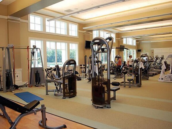 Un gimnasio con diversas máquinas de ejercicio, amplias ventanas y un techo alto.