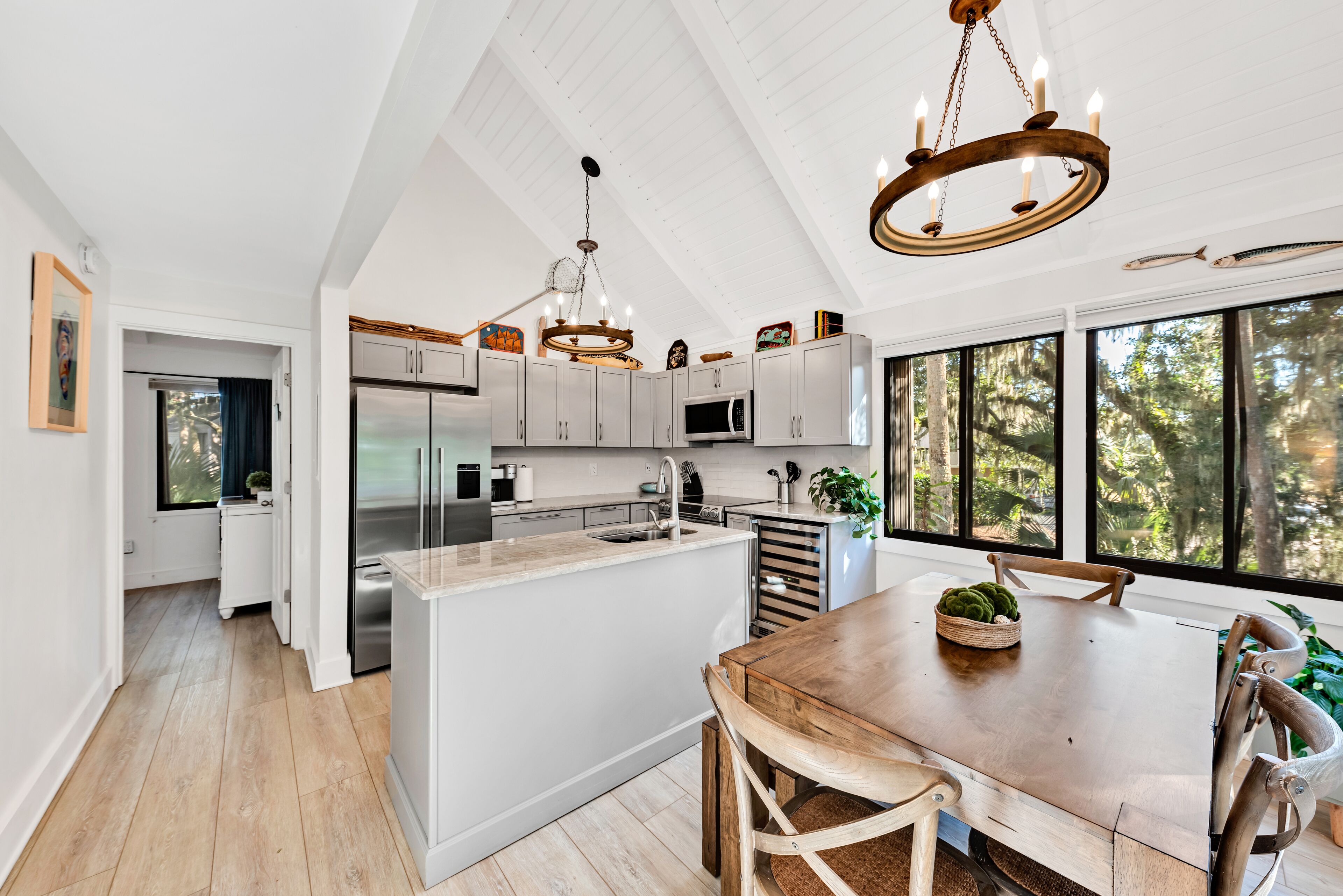A spacious kitchen with white cabinetry, a wooden island, and a large window offering a view of trees.