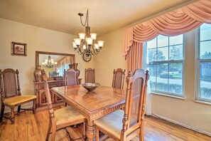 Comedor con mesa de madera, sillas, candelabro y ventanas grandes con cortinas.
