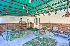 Un patio al aire libre con mesa de vidrio, sillas de metal, un banco y una decoración floral colgante.
