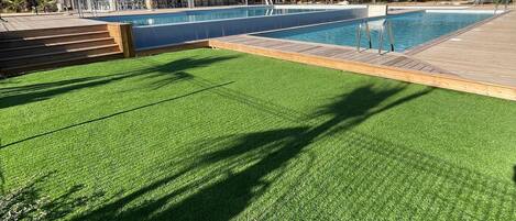 A swimming pool with a wooden deck and a glass-enclosed lounge area.