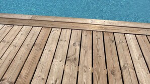 A clear swimming pool with wooden deck in the foreground and a building in the background.