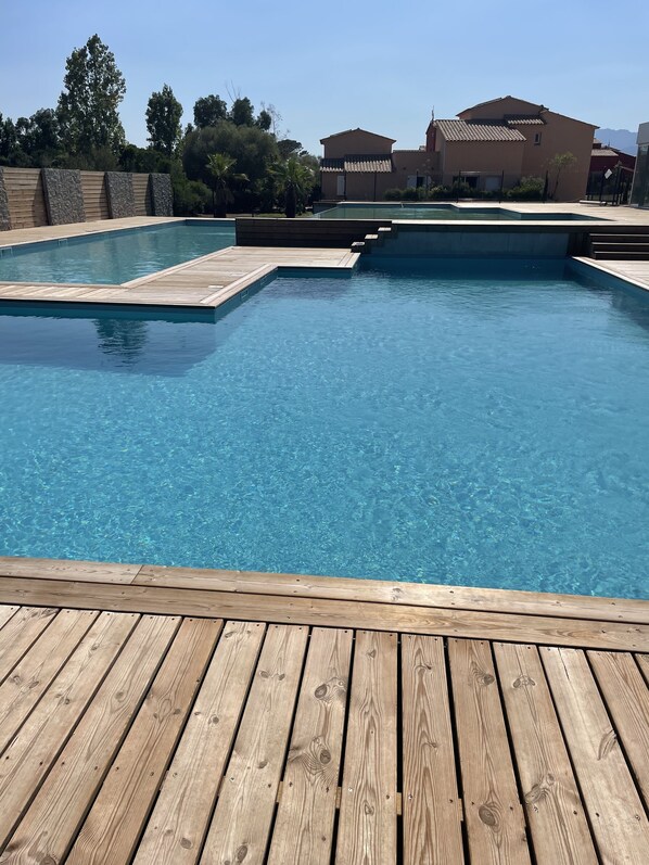 A clear swimming pool with wooden deck in the foreground and a building in the background.