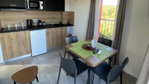A modern kitchen with a microwave, sink, and wooden cabinets. There is a dining table with chairs and a view of greenery outside.
