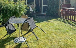 A patio with a round table and four chairs, surrounded by a wooden fence and greenery.