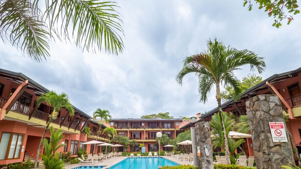 Ein Hotel mit Swimmingpool, umgeben von Palmen und Liegestühlen.