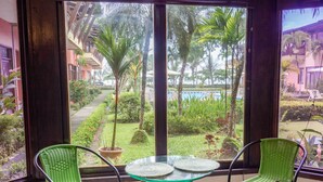 Ein Zimmer mit Glastisch und zwei grünen Korbstühlen, mit Blick auf einen Pool und üppiges Grün.