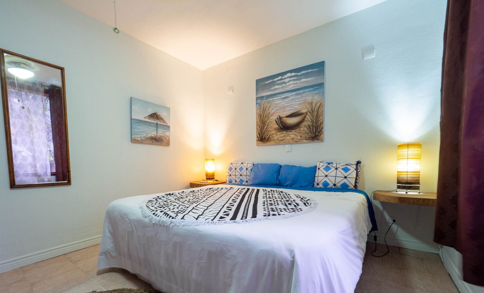 A bedroom with a bed, two wall-mounted lamps, and two paintings.