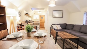 Una sala moderna con un sofá, una mesa de comedor con platos y cubiertos, una planta en maceta y una cocina al fondo.