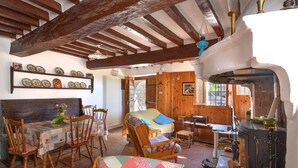 A rustic interior with exposed wooden beams, a dining area with a table and chairs, a cozy seating area with a cushioned chair, and a kitchen area with a stove and utensils. - Pet friendly home in Monchio delle Olle (Monchio delle Olle)