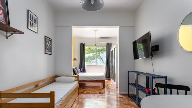 A room with two wooden beds, a TV, a desk, and a large window with curtains. - Studio in Copacabana Ideal for the Family Jc509 (Rio de Janeiro)