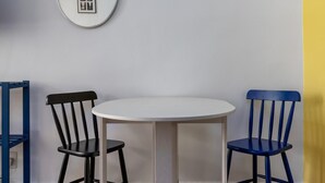A dining area with a round table and two chairs, one black and one blue, on a herringbone wooden floor. - Studio in Copacabana Ideal for the Family Jc509 (Rio de Janeiro)