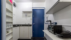 A compact kitchen with white cabinets, a blue door, and a microwave on a white countertop. - Studio in Copacabana Ideal for the Family Jc509 (Rio de Janeiro)