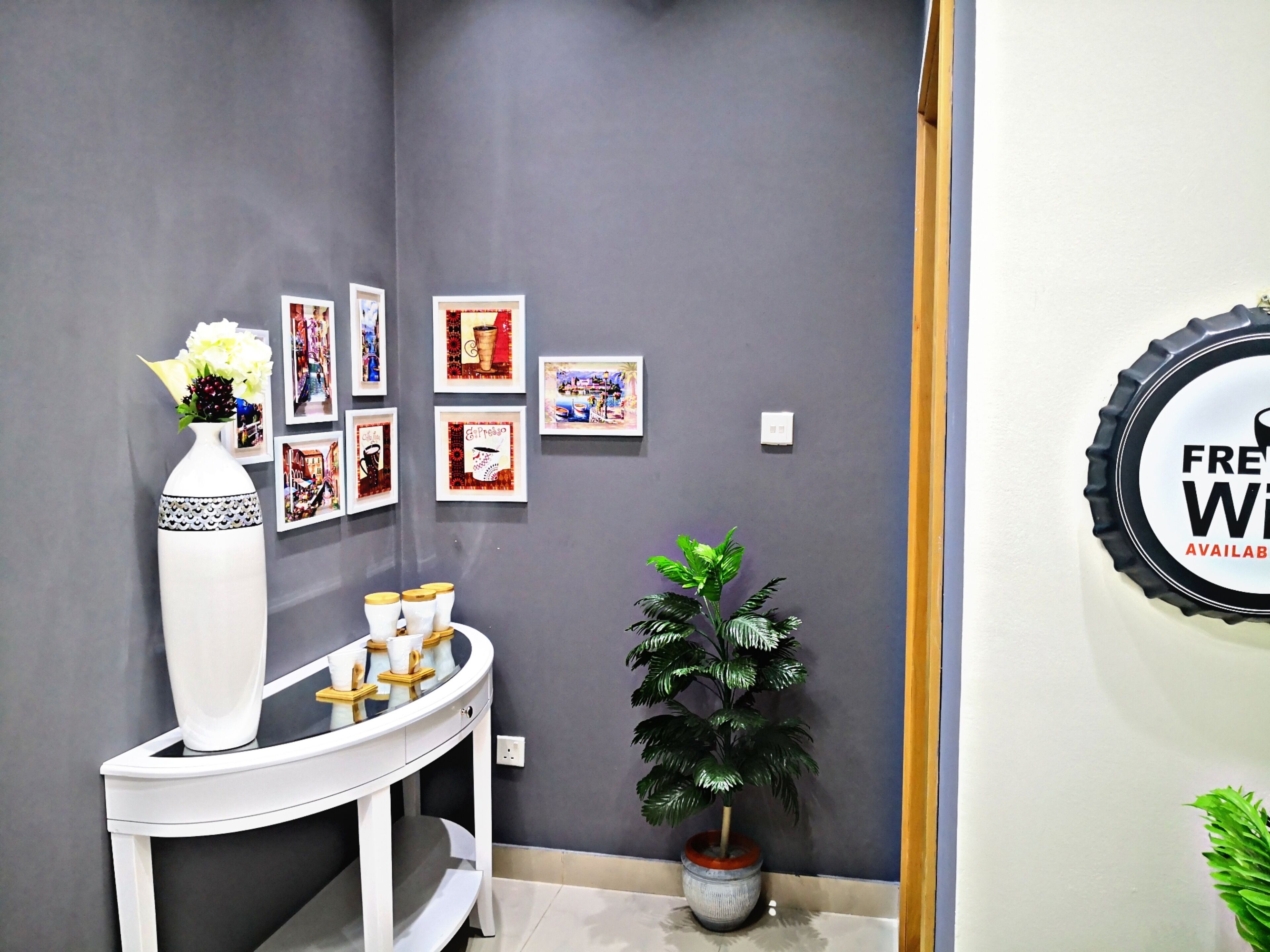 A room with a grey wall, a white console table with decorative items, a potted plant, and framed artwork.