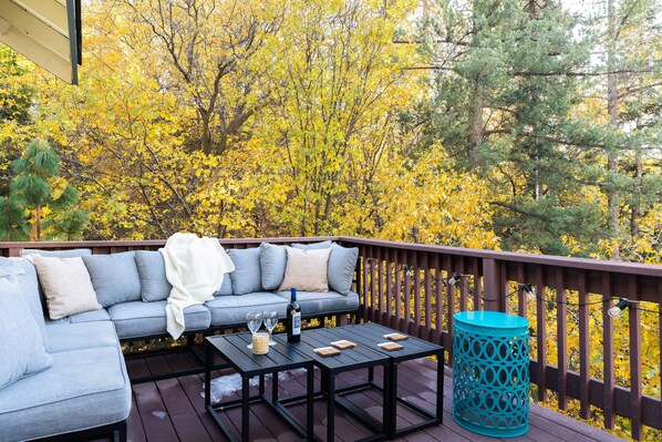 A deck with a gray sofa, a black coffee table, and a blue trash can.