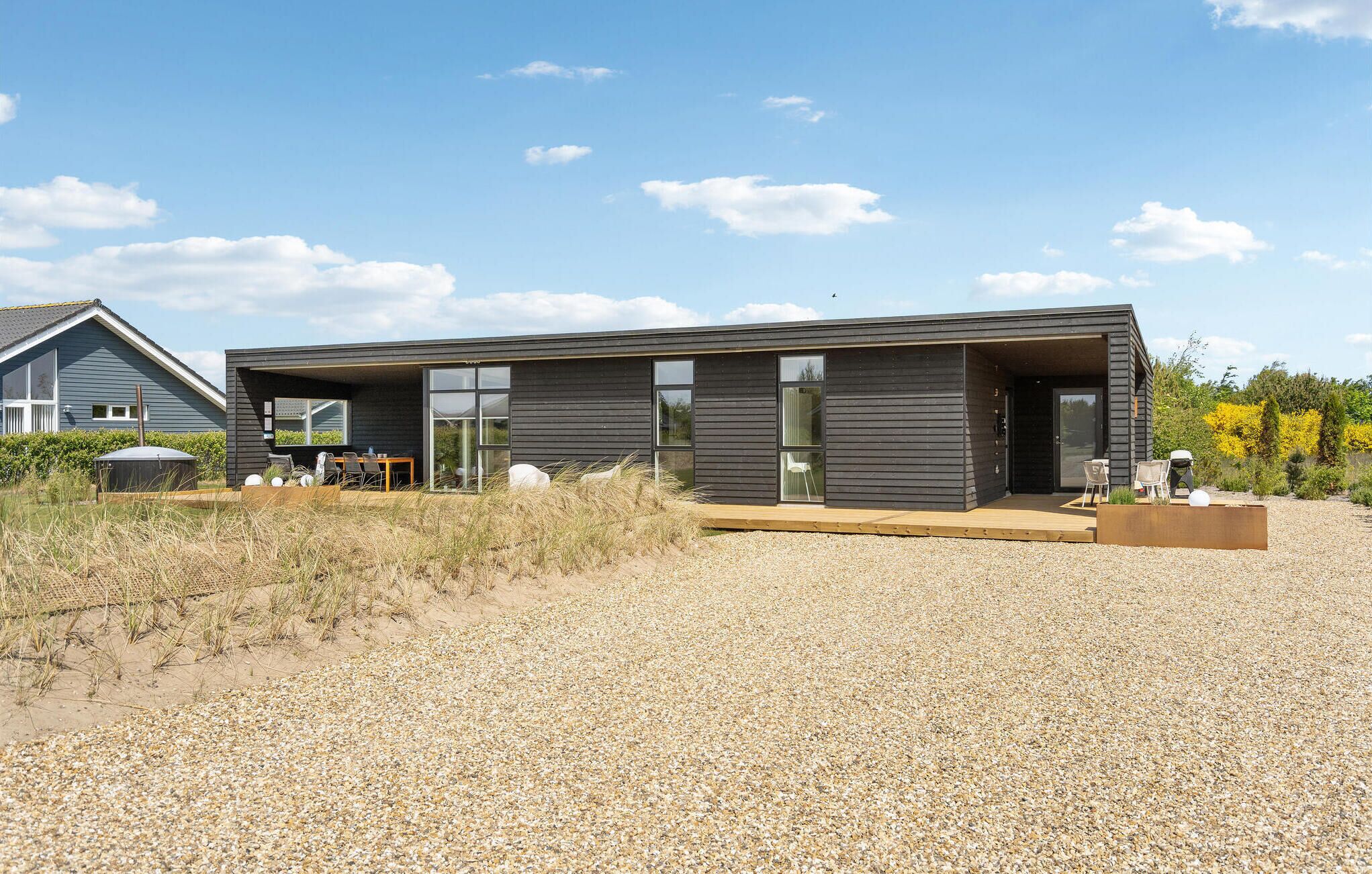 A modern two-story house with a gravel driveway and a wooden deck.