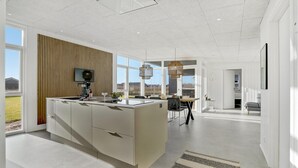 A modern kitchen with a large island, a dining area with a view, and a living space with a sofa and a TV. - Cozy home in Tarm with WiFi (Tarm)