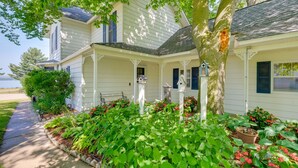 A house with a porch, a birdhouse, and a garden with various plants. - Elegant 1905 Home: Steps to Torch Lake & Dtwn (Alden)