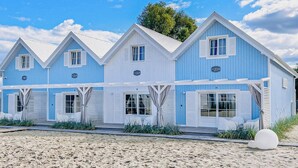 A row of blue and white beach houses with numbered doors, a sandy beach in front, and a clear sky. - Stunning home in Mielno (Mielno)