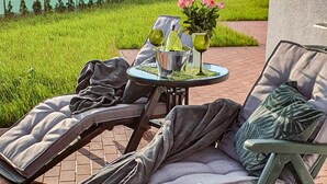 A patio with two reclining chairs, a small table with a metal bucket, and a vase with pink flowers. - Nice home in Slowienkowo with WiFi (Slowienkowo)