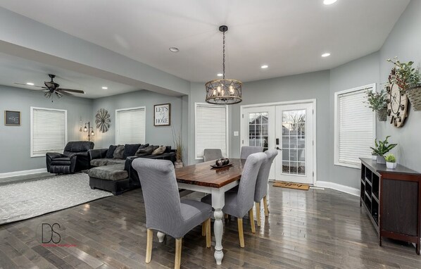A spacious living room with a dark wood floor, grey upholstered furniture, and a dining area with a wooden table and grey chairs.