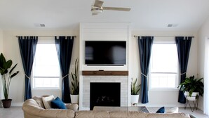 Una sala de estar moderna con chimenea, un televisor de pantalla plana grande y un ventilador de techo.