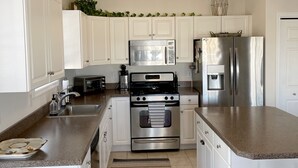 Una cocina moderna con gabinetes blancos, electrodomésticos de acero inoxidable, una encimera de granito y una lámpara colgante.