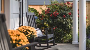 A porch with a rocking chair, a wooden fence, and a garden with red flowers.