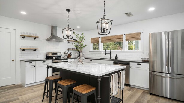 A modern kitchen with a central island, bar stools, stainless steel appliances, and pendant lighting.