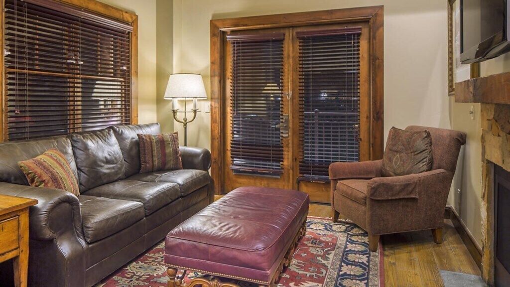 A living room with a leather sofa, a matching ottoman, a brown armchair, and a patterned rug.