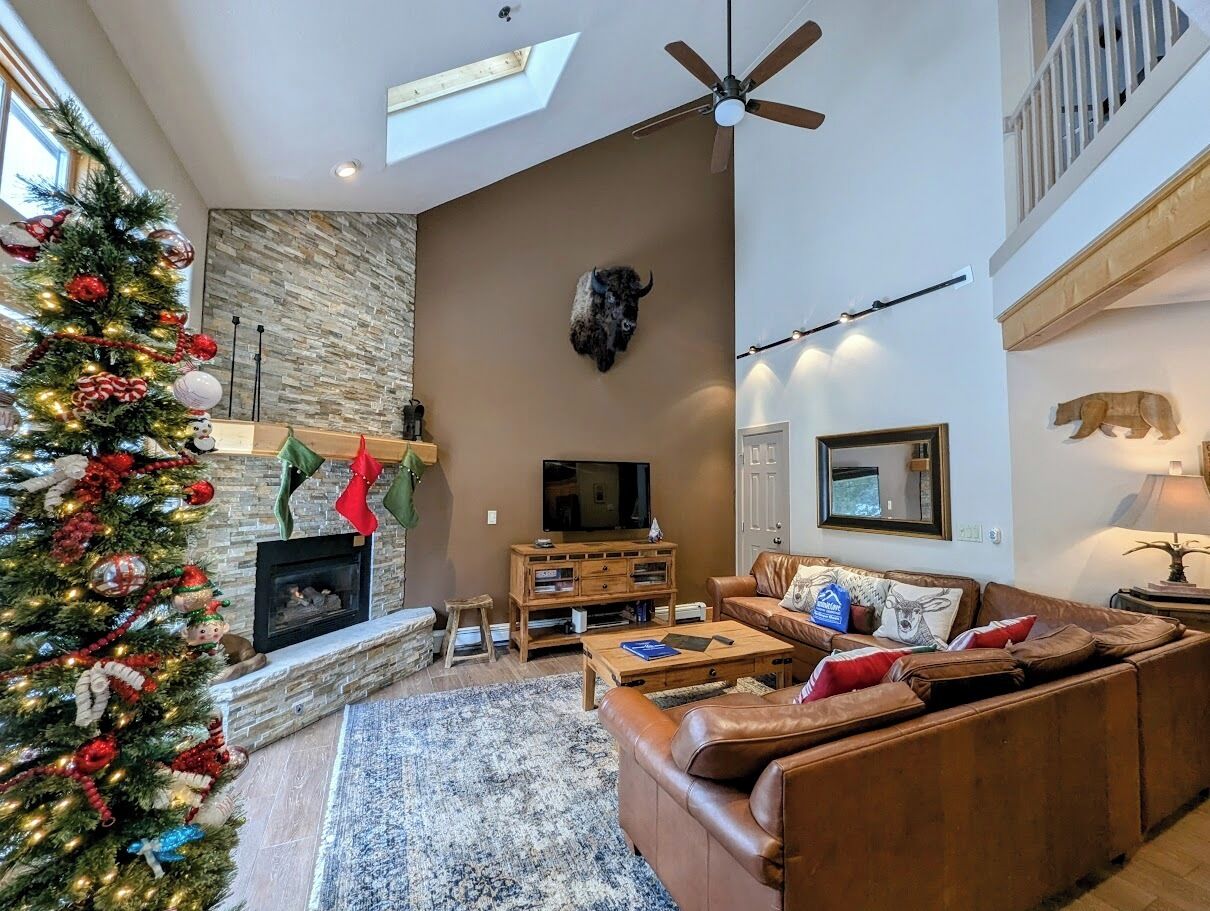 A spacious living room with a fireplace, leather sofa, and a Christmas tree.