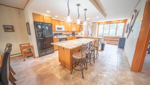 A modern kitchen with wooden cabinets, a central island with bar stools, stainless steel appliances, and pendant lighting. - Pines 2089 (Keystone)
