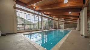 An indoor swimming pool with a view of mountains through large windows, wooden beams on the ceiling, and a tiled floor. - Pines 2089 (Keystone)