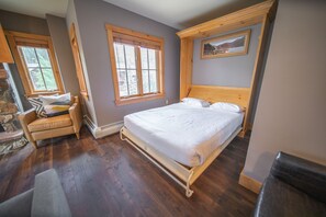 A bedroom with a wooden bed, two windows, a stone fireplace, and a wooden ceiling. - Expedition Station 8593 (Keystone)