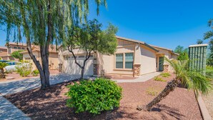 A residential house with a garage, a driveway, and a well-maintained garden with a palm tree and shrubs. - Gorgeous & Comfy Family Getaway ~ Games ~ Backyard (Surprise)