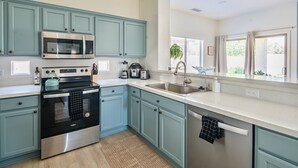 A modern kitchen with teal cabinets, stainless steel appliances, and a large window providing natural light. - Gorgeous & Comfy Family Getaway ~ Games ~ Backyard (Surprise)