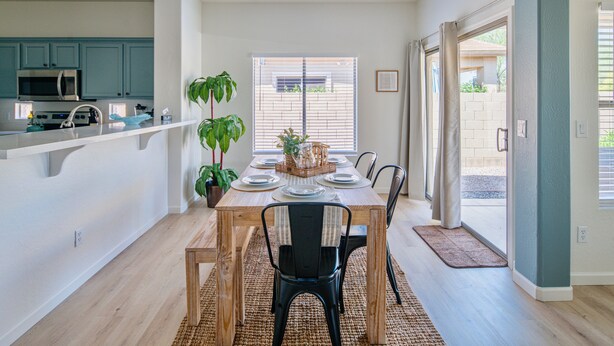 A dining area with a wooden table set for four, surrounded by chairs, a potted plant, and a view through a window with blinds. - Gorgeous & Comfy Family Getaway ~ Games ~ Backyard (Surprise)