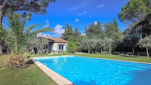 Une piscine avec une maison en arrière-plan, le tout entouré d’arbres.